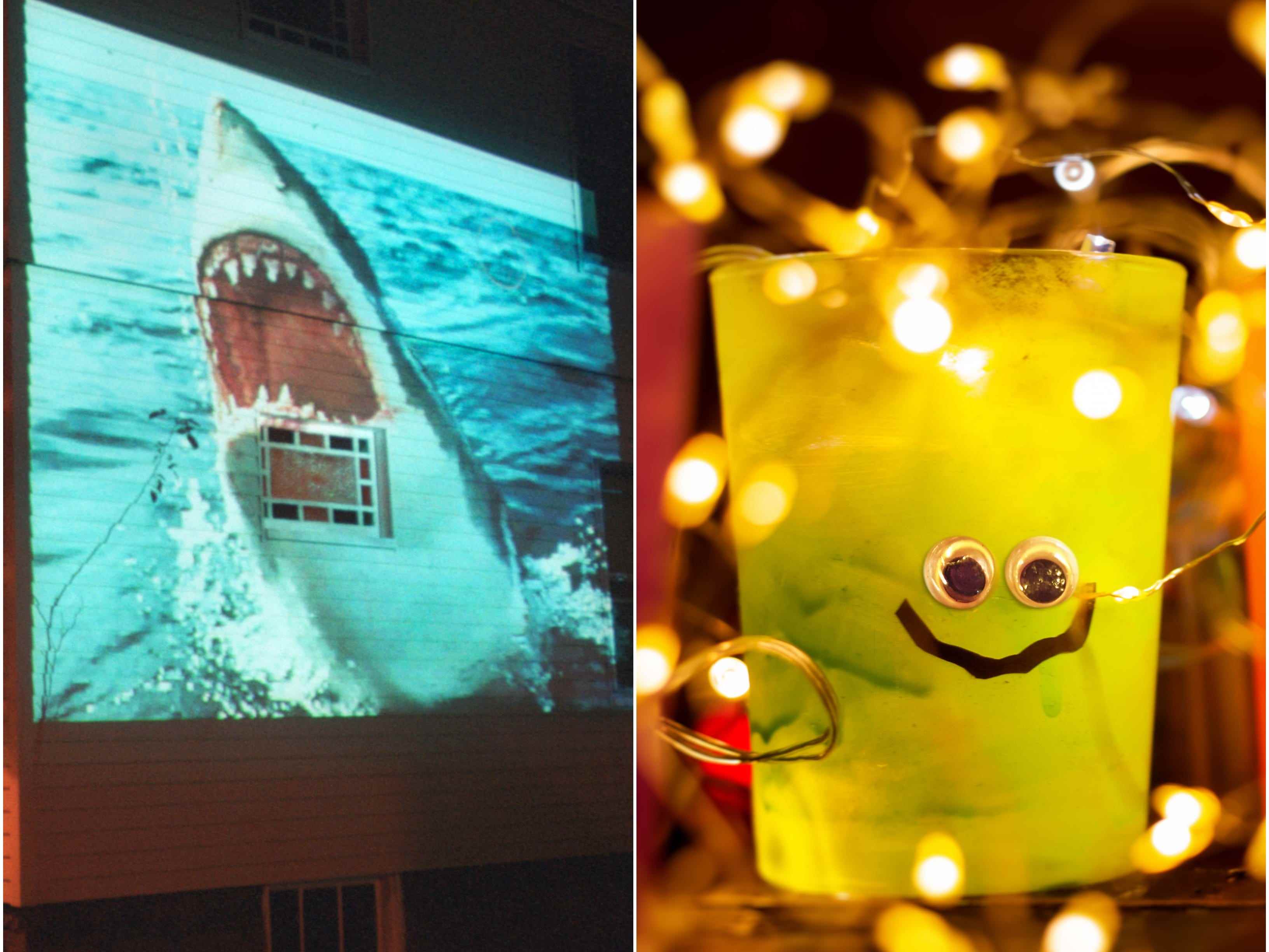Ein Hai wird vor Halloween auf ein Haus projiziert, während eine Herbstdekoration von Lichtern umgeben ist.