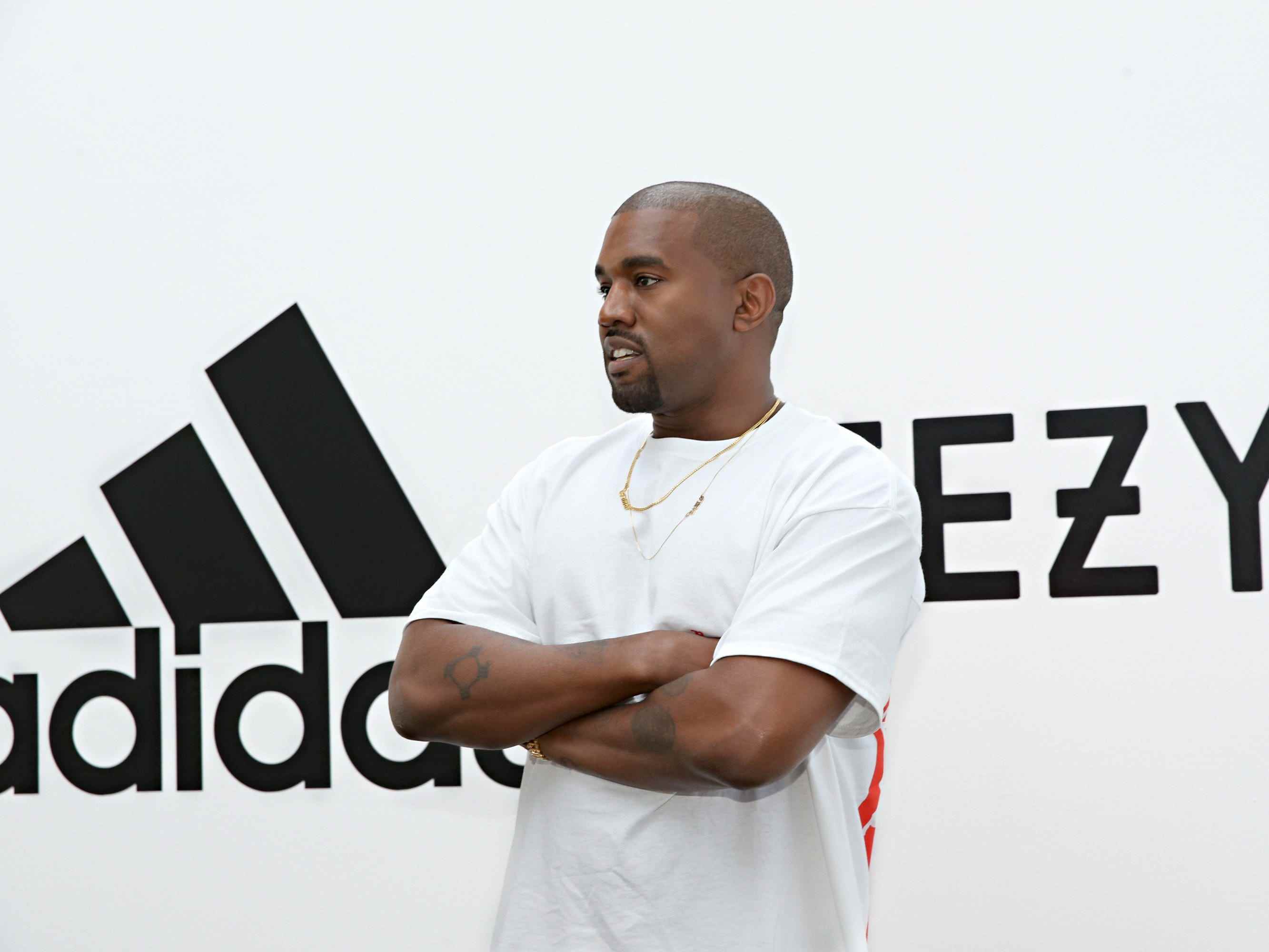 Kanye West vor den Logos von Yeezy und Adidas