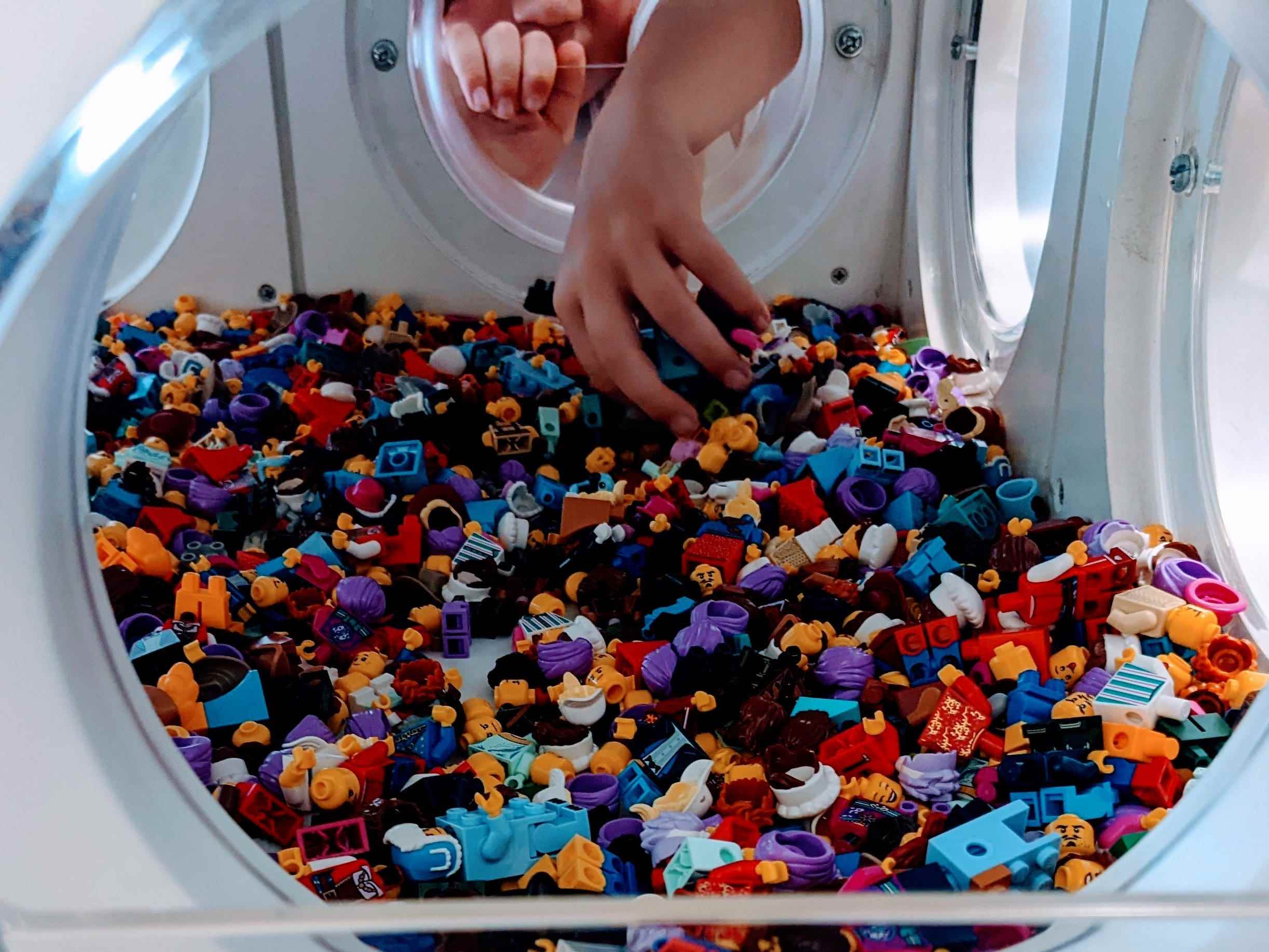 Hand, die in einen Behälter voller kleiner Legofiguren im Lego Store in Disney Springs greift
