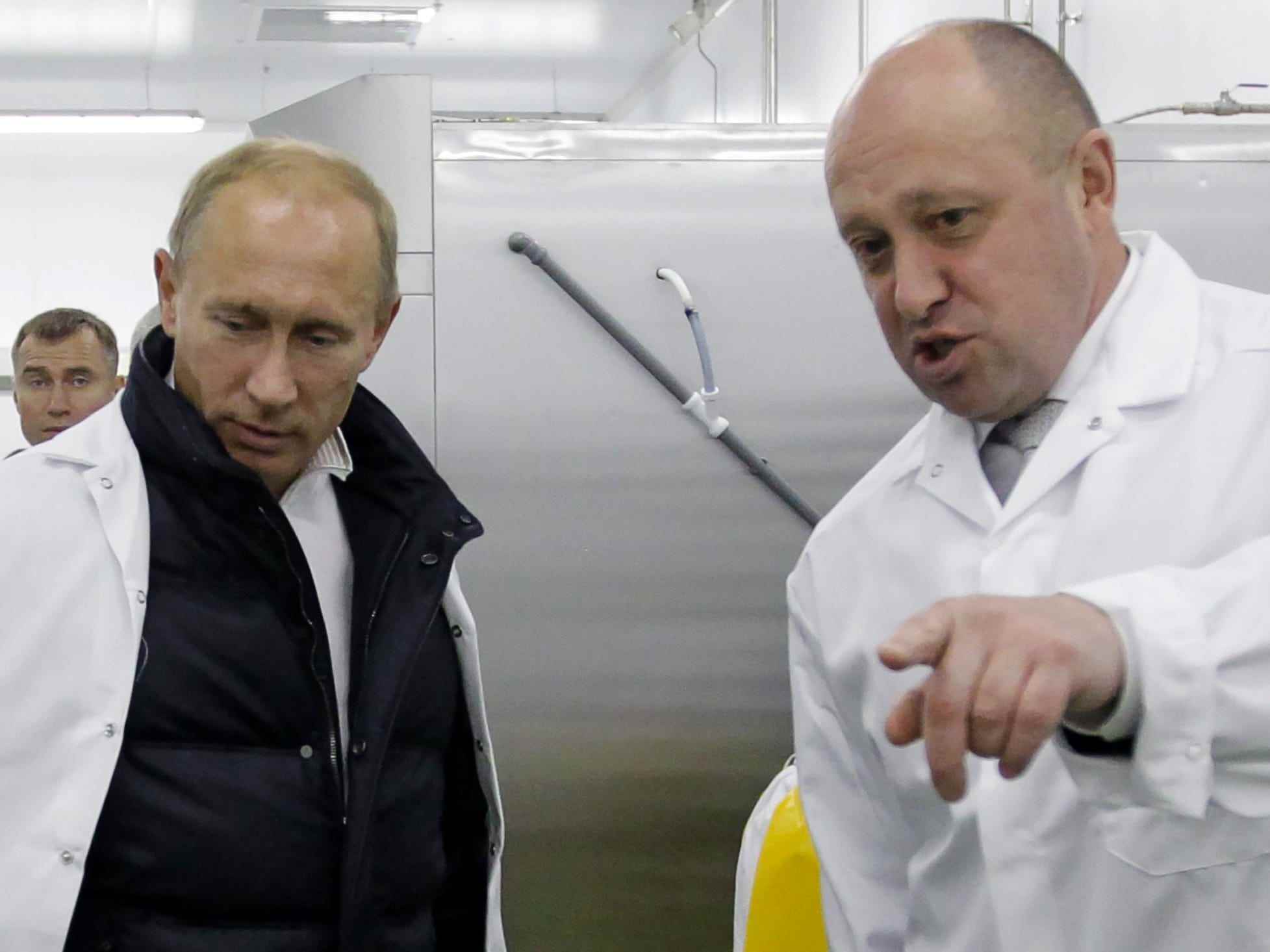Putin und Prigozhin in weißen Kitteln, wobei letzterer auf etwas außerhalb der Kamera zeigt