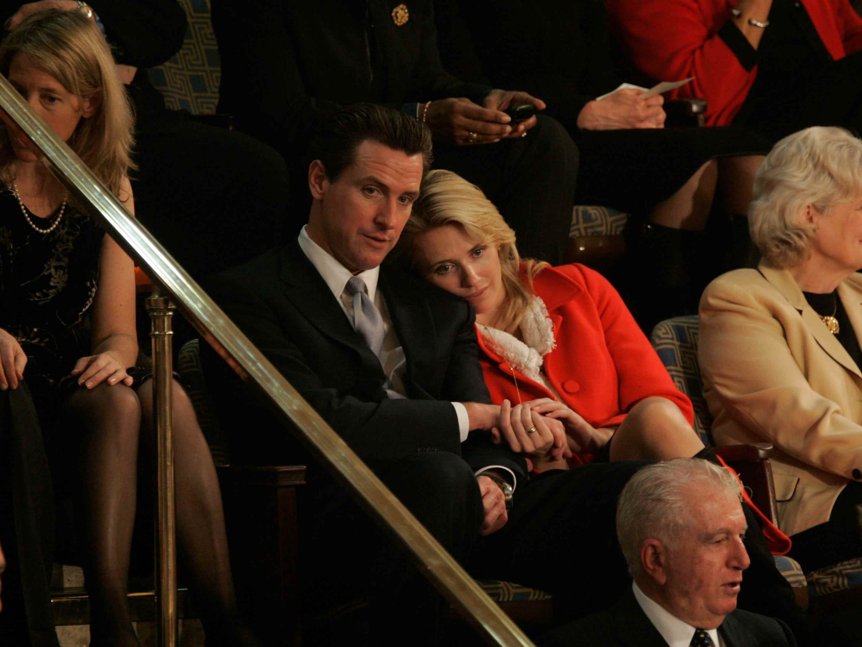 Jennifer Siebel Newsom und Gavin Newsom kuscheln, während sie sich eine politische Zeremonie ansehen.
