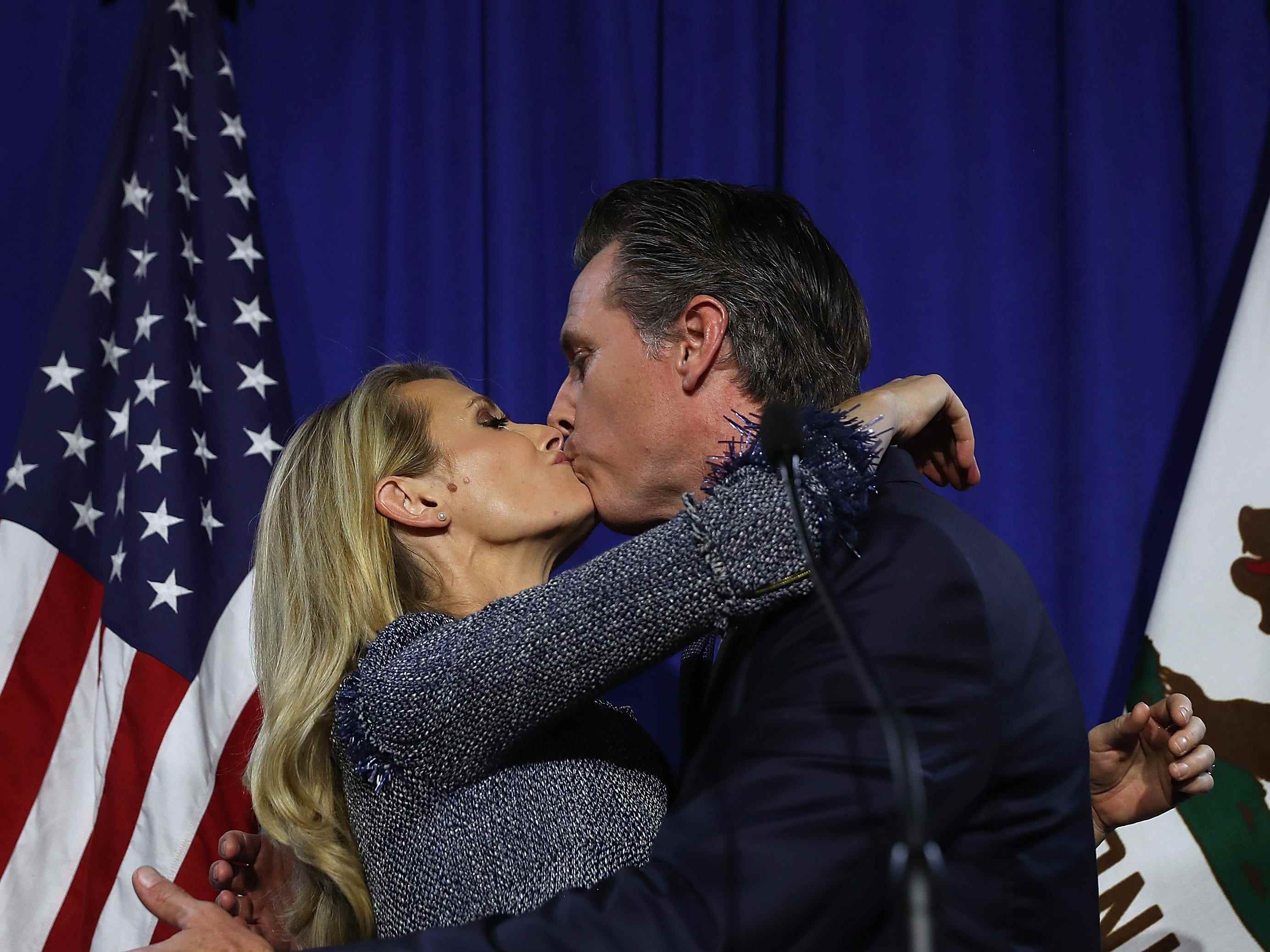 Jennifer Siebel Newsom und Gavin Newsom küssen sich vor einer amerikanischen Flagge.