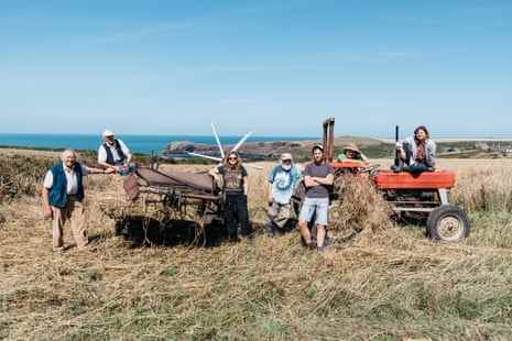 Sieben Mitglieder des Llafur Ni-Netzwerks, darunter Gerald Miles, Iwan Evans und Owen Shiers, lächeln, während sie neben einem Schneidebinder und einem Traktor auf einem Feld stehen oder darauf sitzen