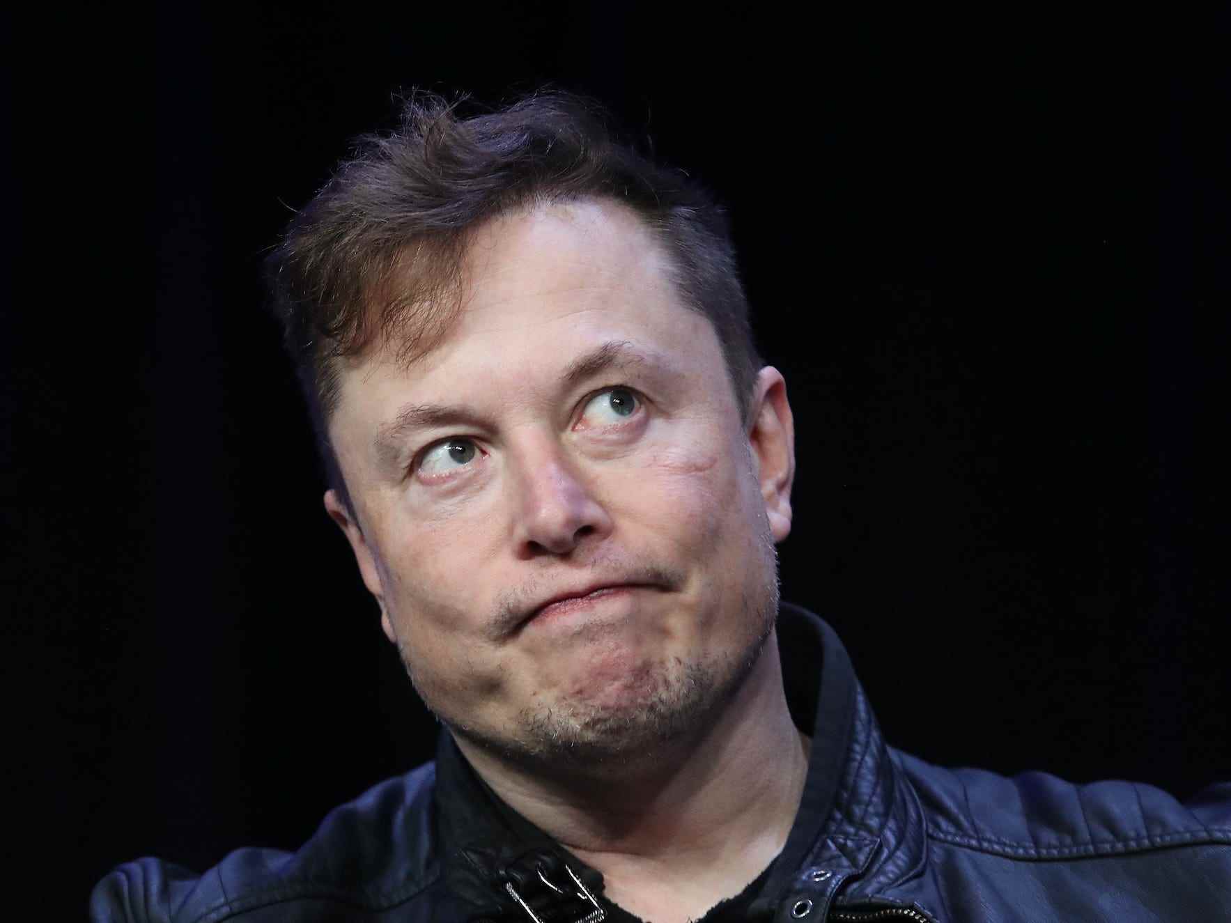 Elon Musk verzieht das Gesicht, während er vor schwarzem Hintergrund zur Seite schaut