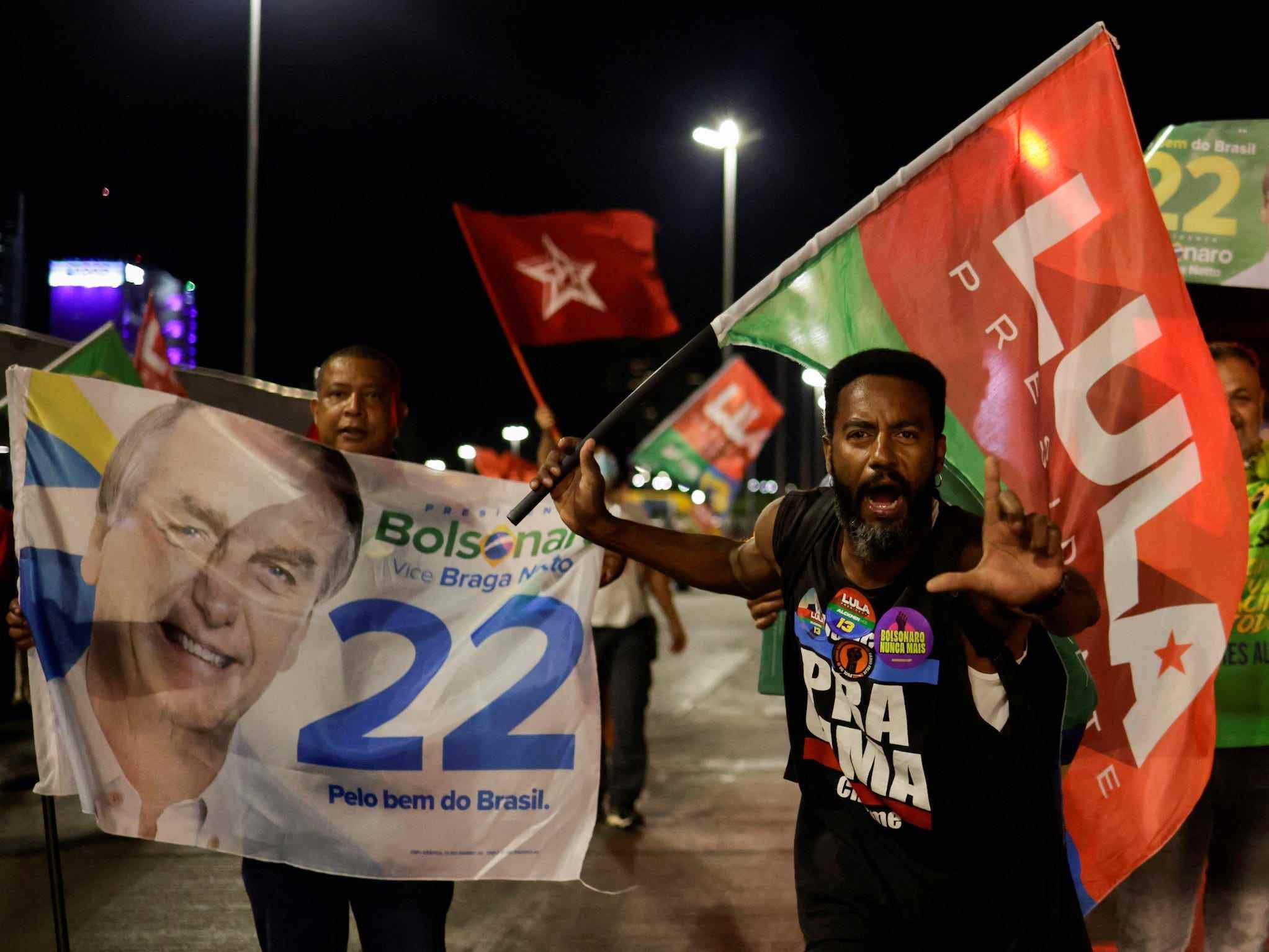 Menge von Menschen, die Fahnen schwenken, einige unterstützen jar bolsonaro, einige unterstützen Luiz Inacio Lula da Silva, ein Mann, der nachts die Finger in L-Form hält