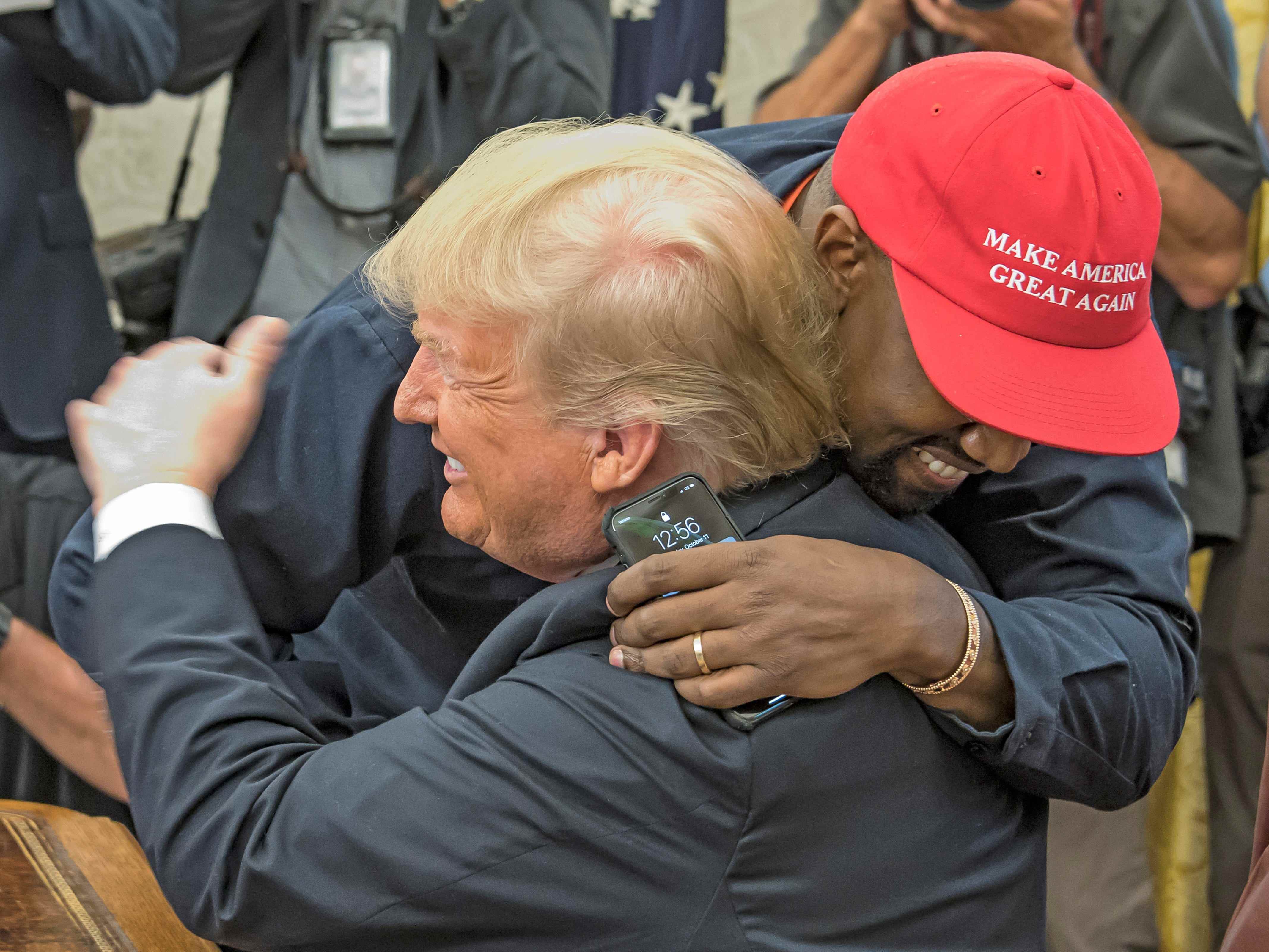 Kanye West, in einem roten MAGA-Hut, umarmt DOnald Trump im Oval Office.