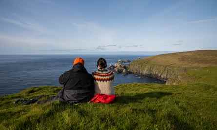 Ein Paar sitzt auf einer Klippe und bewundert die Landschaft w Hermaness National Nature Reserve, Unst Island, Shetlands.