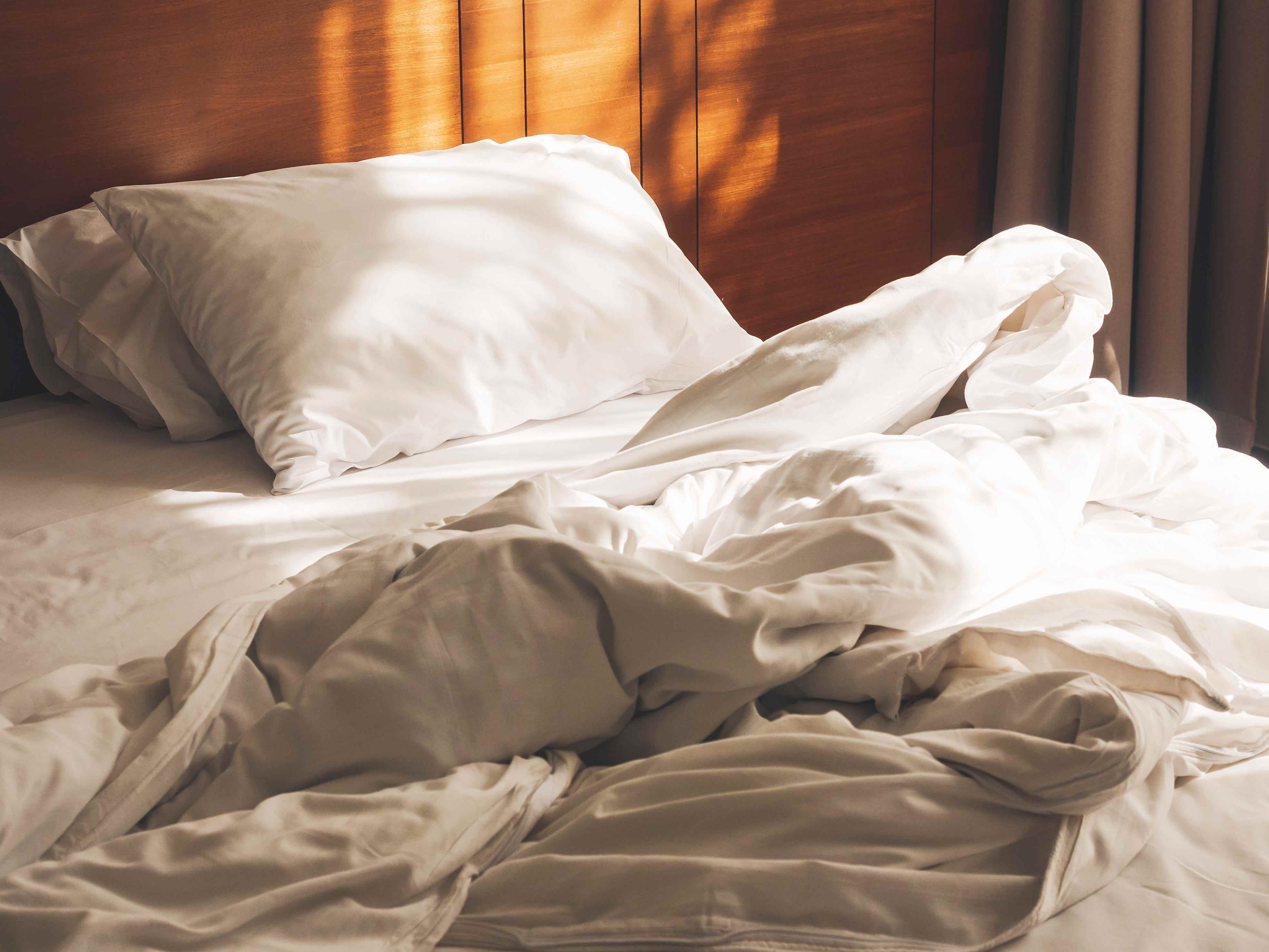 Bett mit grau-weißer Bettwäsche und Kopfteil aus Holz