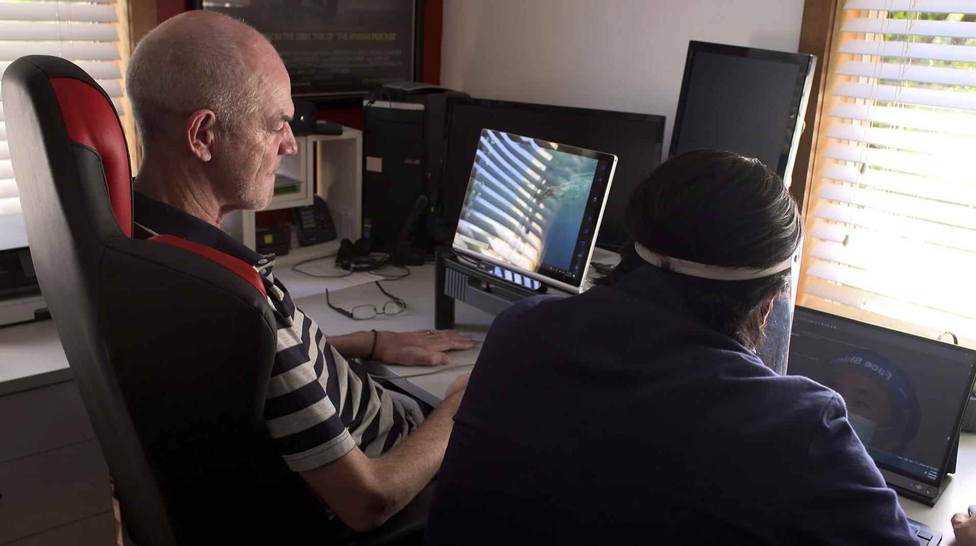 mann mit gehirn computerschnittstelle sitzt am computer - hände auf dem schreibtisch, steuert ihn mit seinem gedanken