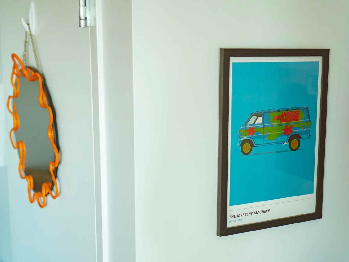 An den Wänden hängen ein Spiegel mit einem orangefarbenen Kringel-Rahmen und ein Druck der mysteriösen Maschine aus „Scooby-Doo“.