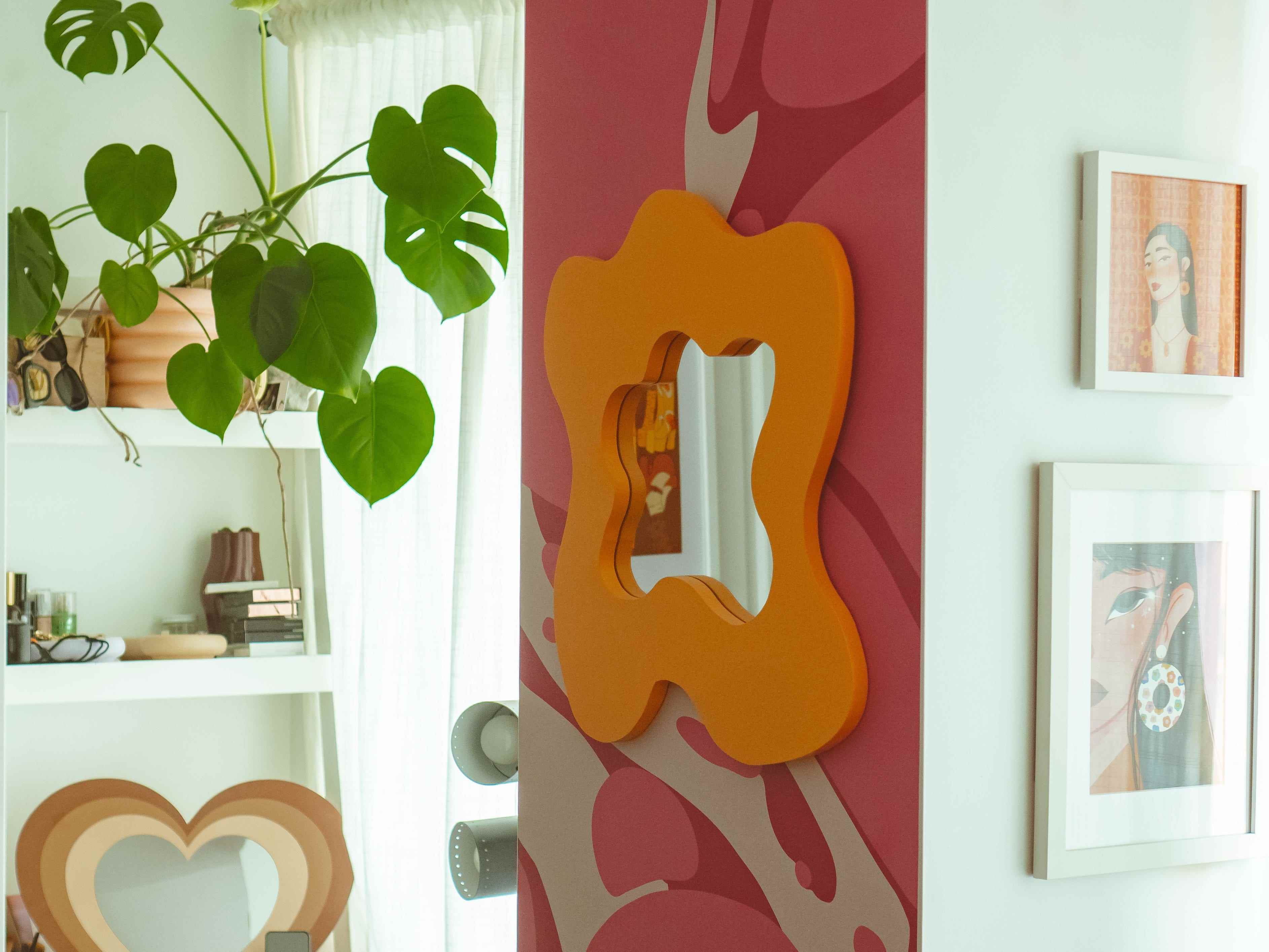 Rosa und rote abstrakte Tapete an einer Wand mit einem groovigen orangefarbenen Spiegel darauf