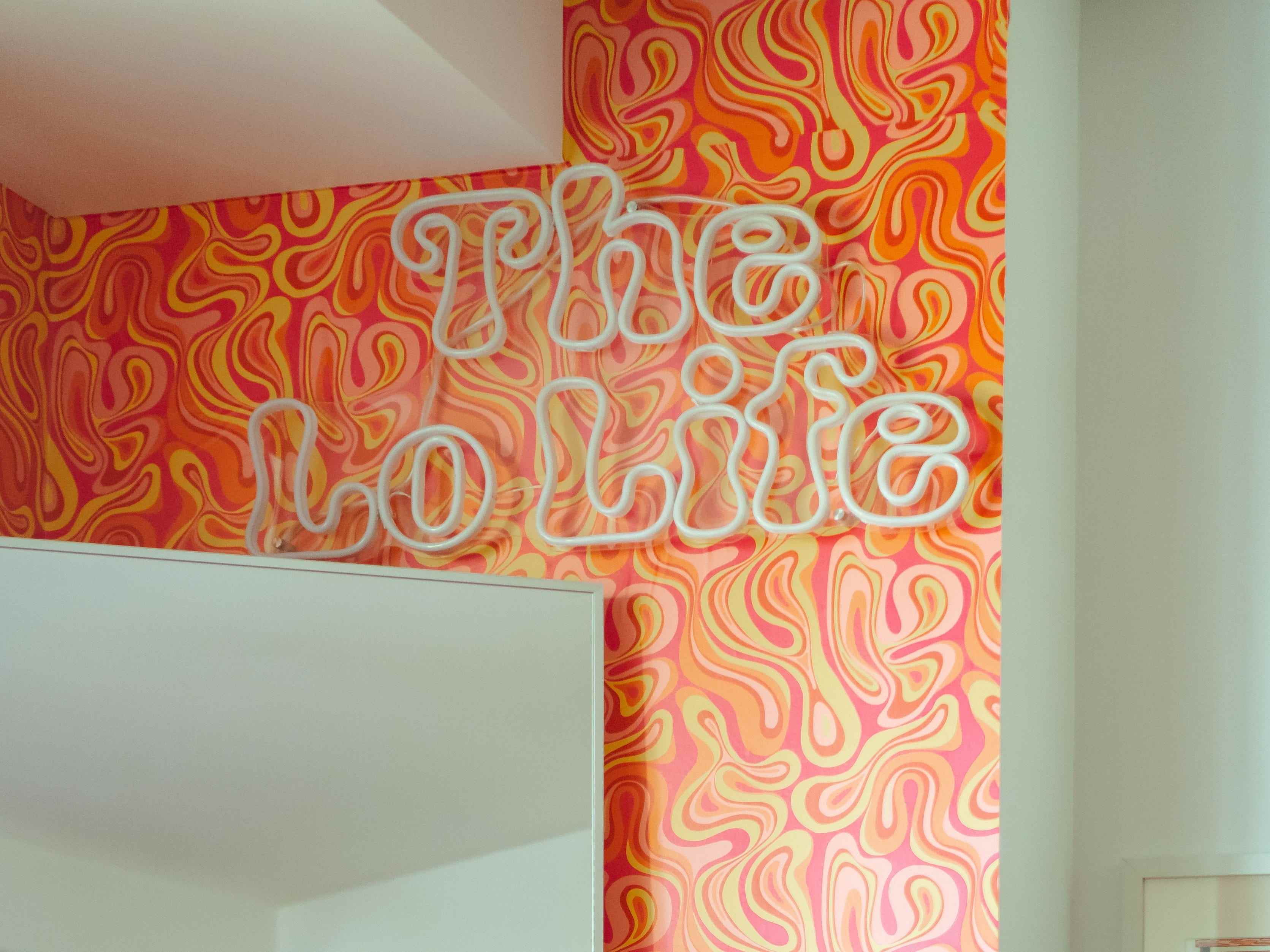 Ein Neonschild „The Lo Life“ an einer Wand mit orangefarbener Wirbeltapete