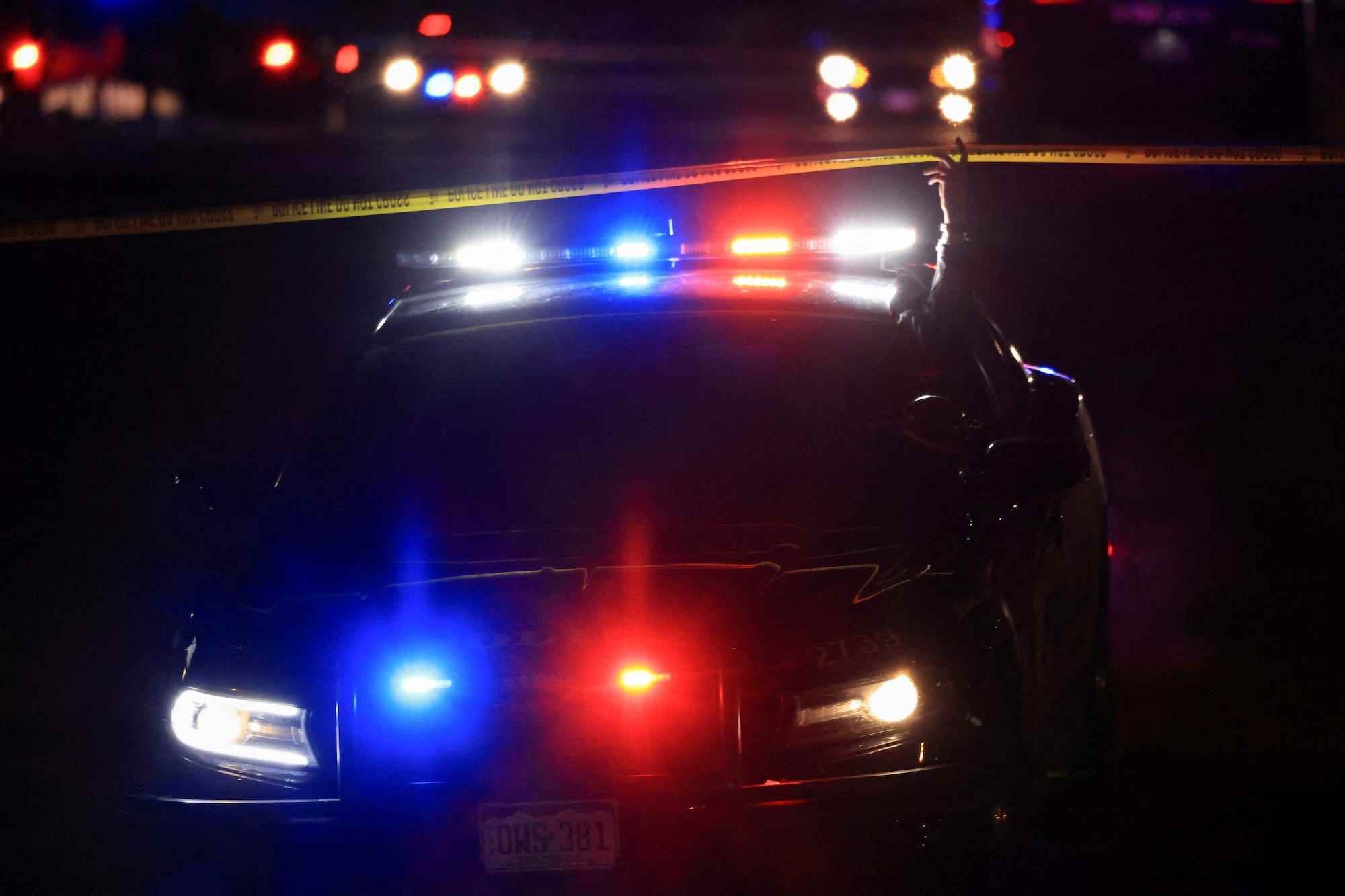 Ein Polizeibeamter aus Colorado Springs hebt nachts eine gelbe Absperrung vor einem Polizeifahrzeug, als sie am frühen 20. November 2022 den Schauplatz einer Schießerei im LGBTQ-Club Club Q besuchen