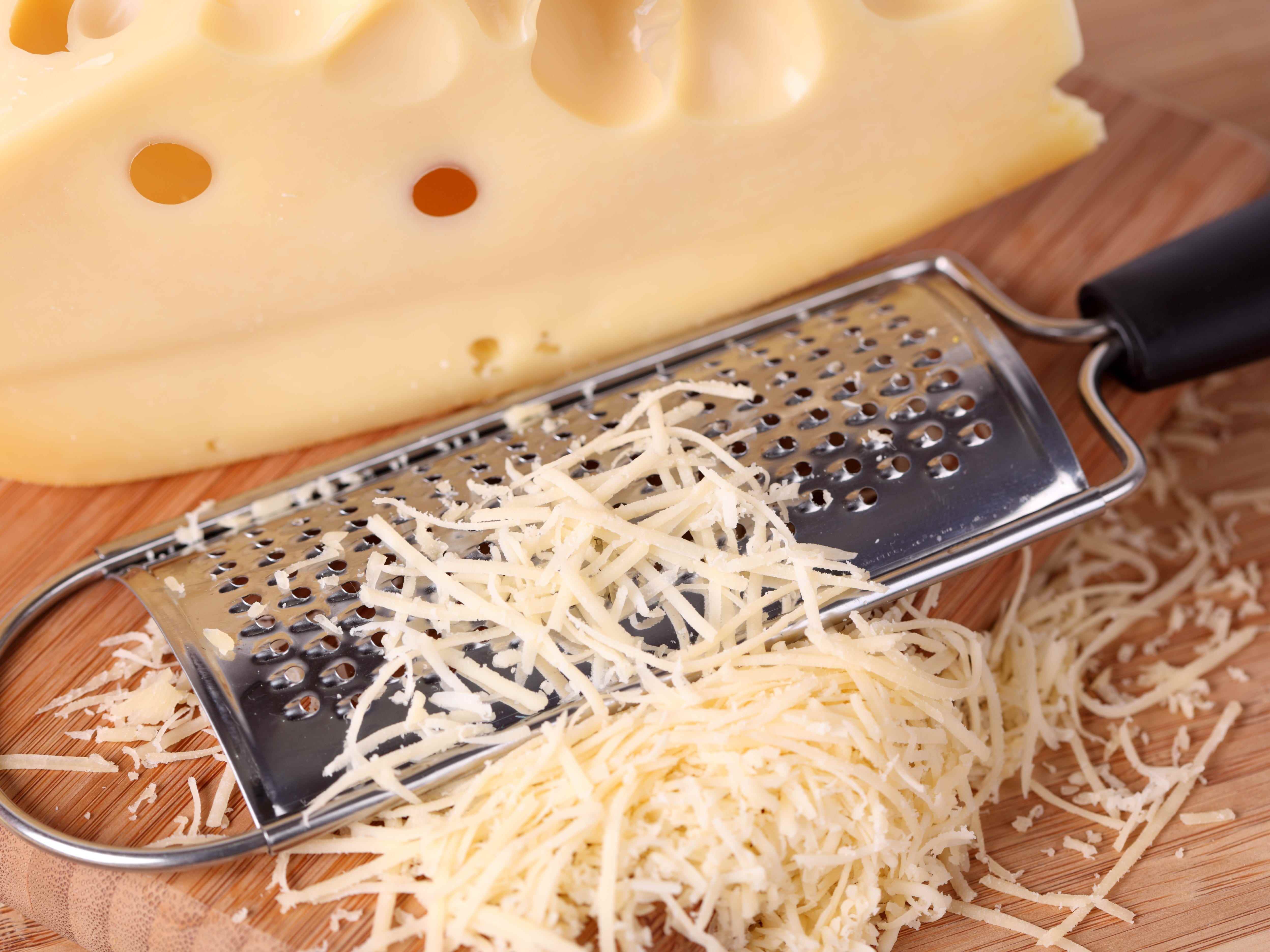 Käseblock neben Stapel geriebenem Käse und Metallreibe