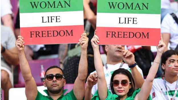 Zwei Iran-Fans halten Transparente mit der Aufschrift „Women Life Freedom“ hoch