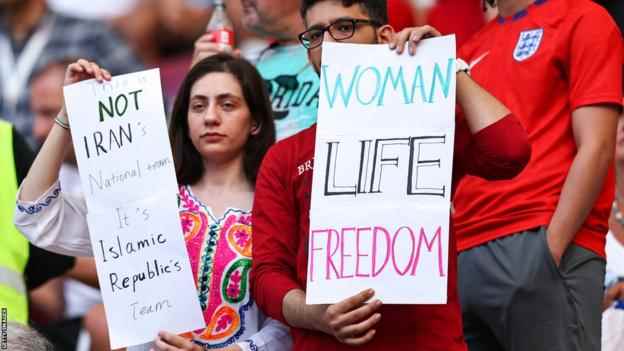Zwei Iran-Fans halten Transparente mit der Aufschrift „Women Life Freedom“ hoch