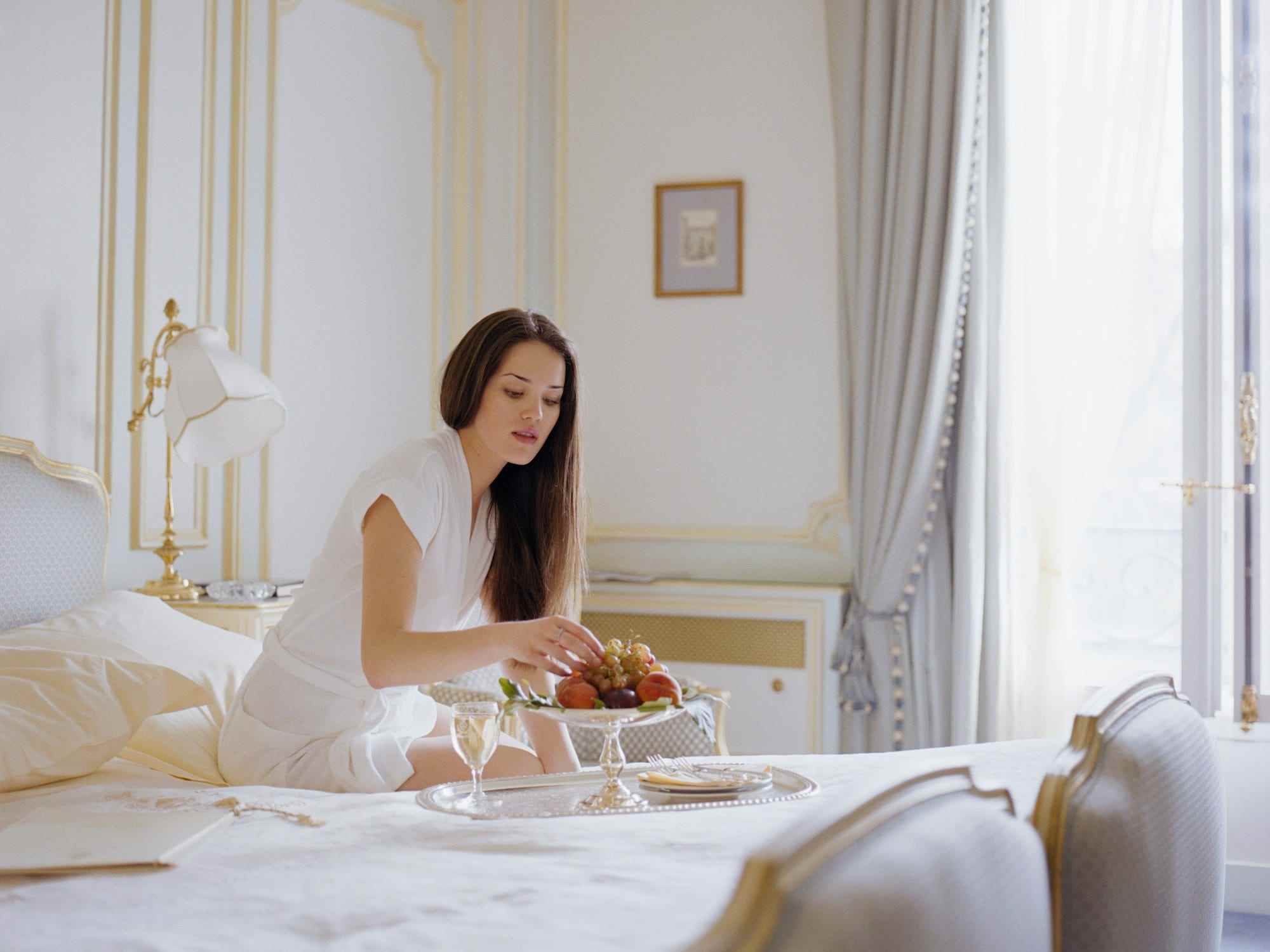 Eine Frau sitzt auf einem Bett in einem Schlafzimmer mit weißen Wänden mit Goldrand.