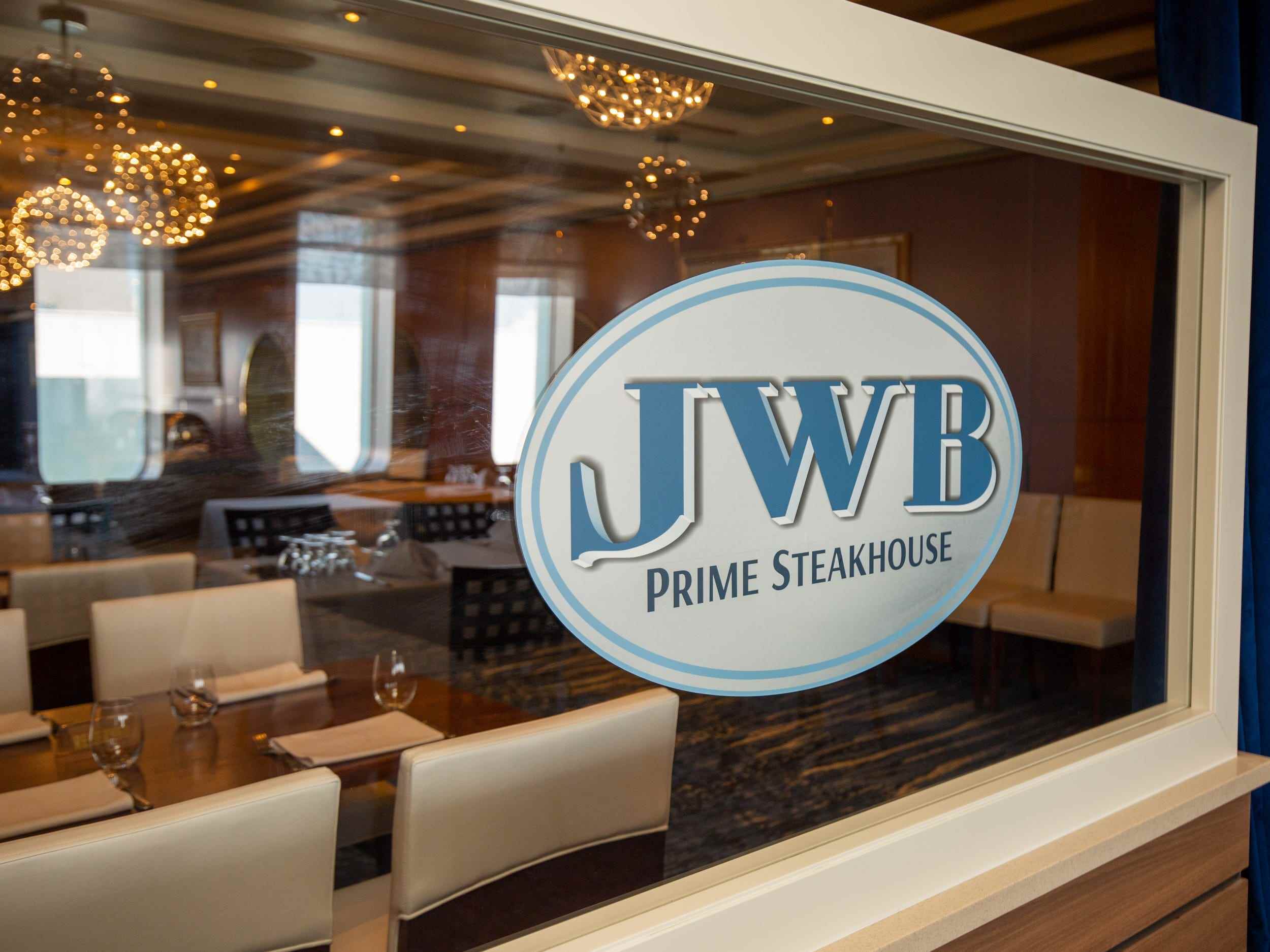 Eine Glasscheibe mit der Aufschrift „JWB Prime Steakhouse“ mit Tischen im Hintergrund.