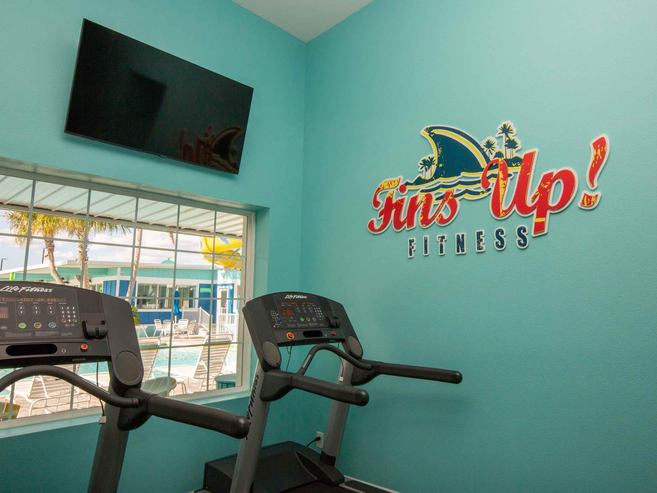 Ein Fitnessbereich mit Laufband, Fernseher, einem Schild mit der Aufschrift „Fins up Fitness“