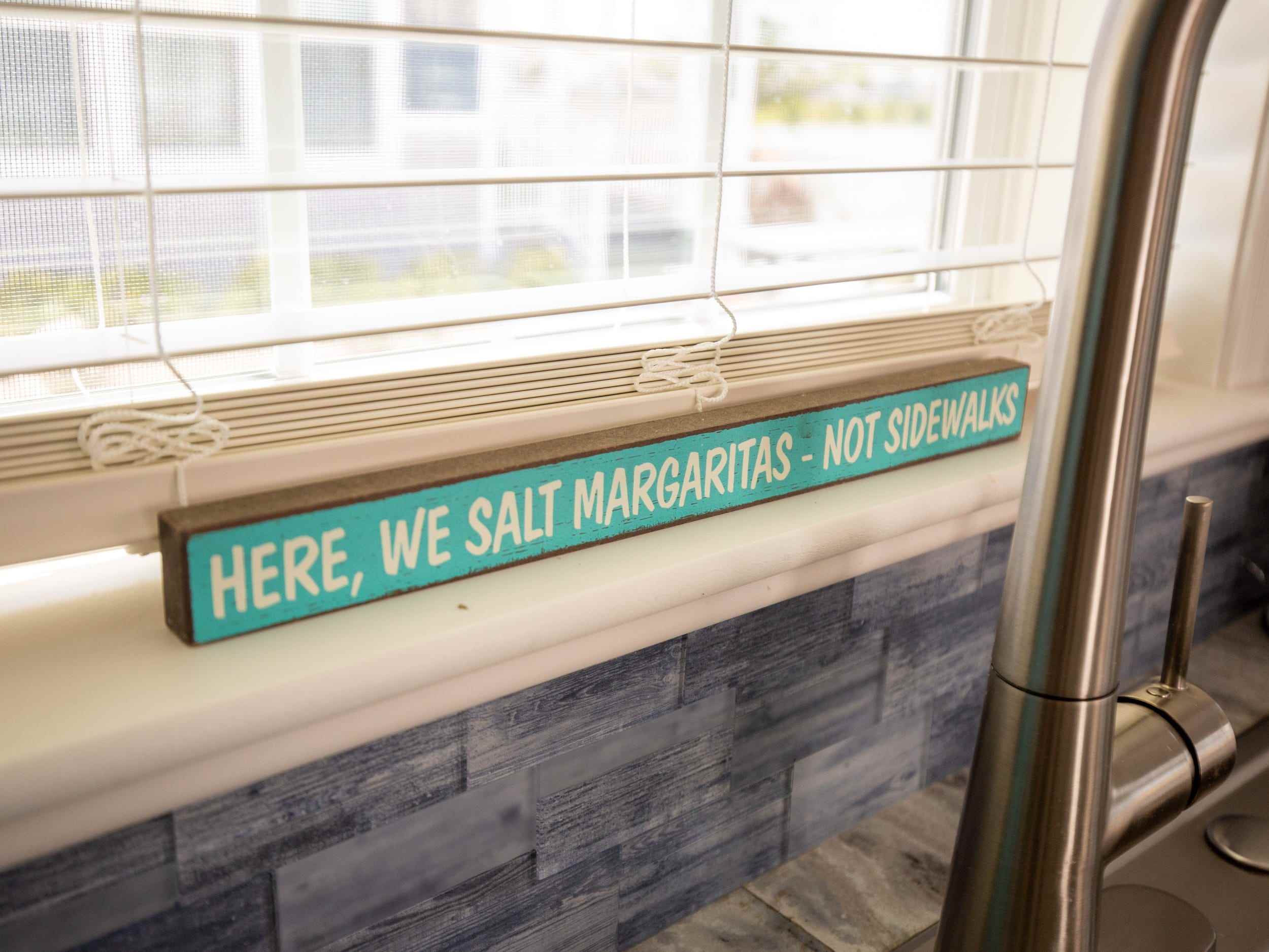 Ein Schild mit der Aufschrift „Hier salzen wir Margaritas, keine Bürgersteige“ unter einem Fenster.