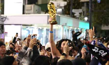 Japanische Fußballfans schwenken nach ihrem Triumph am Mittwochabend in Tokio einen WM-Pokal.