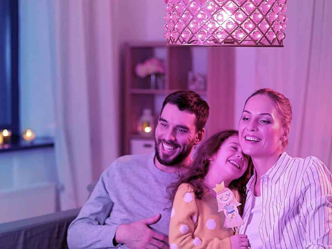 Eine dreiköpfige Familie sitzt in einem Wohnzimmer unter einer rosafarbenen Glühbirne