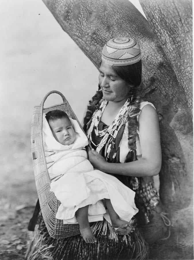 Eine einheimische Hupa-Frau hält ein Baby in einer traditionellen Trage auf ihrem Schoß.