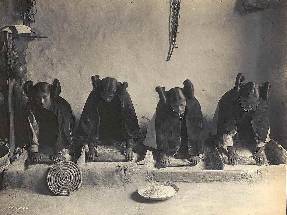 Das Foto zeigt vier junge Hopi-Indianerinnen, die Getreide mahlen.