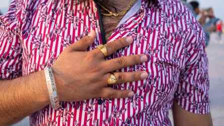 Nahaufnahme eines Wanderarbeiters in Katar in seiner Freizeit in einem rot-weiß gestreiften Hemd mit Goldschmuck an den Fingern.