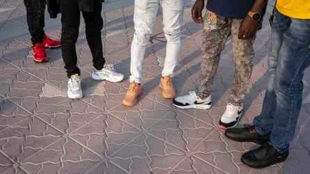 Nahaufnahme der Schuhe und Hosen von fünf Männern an der Corniche in Doha, Katar.