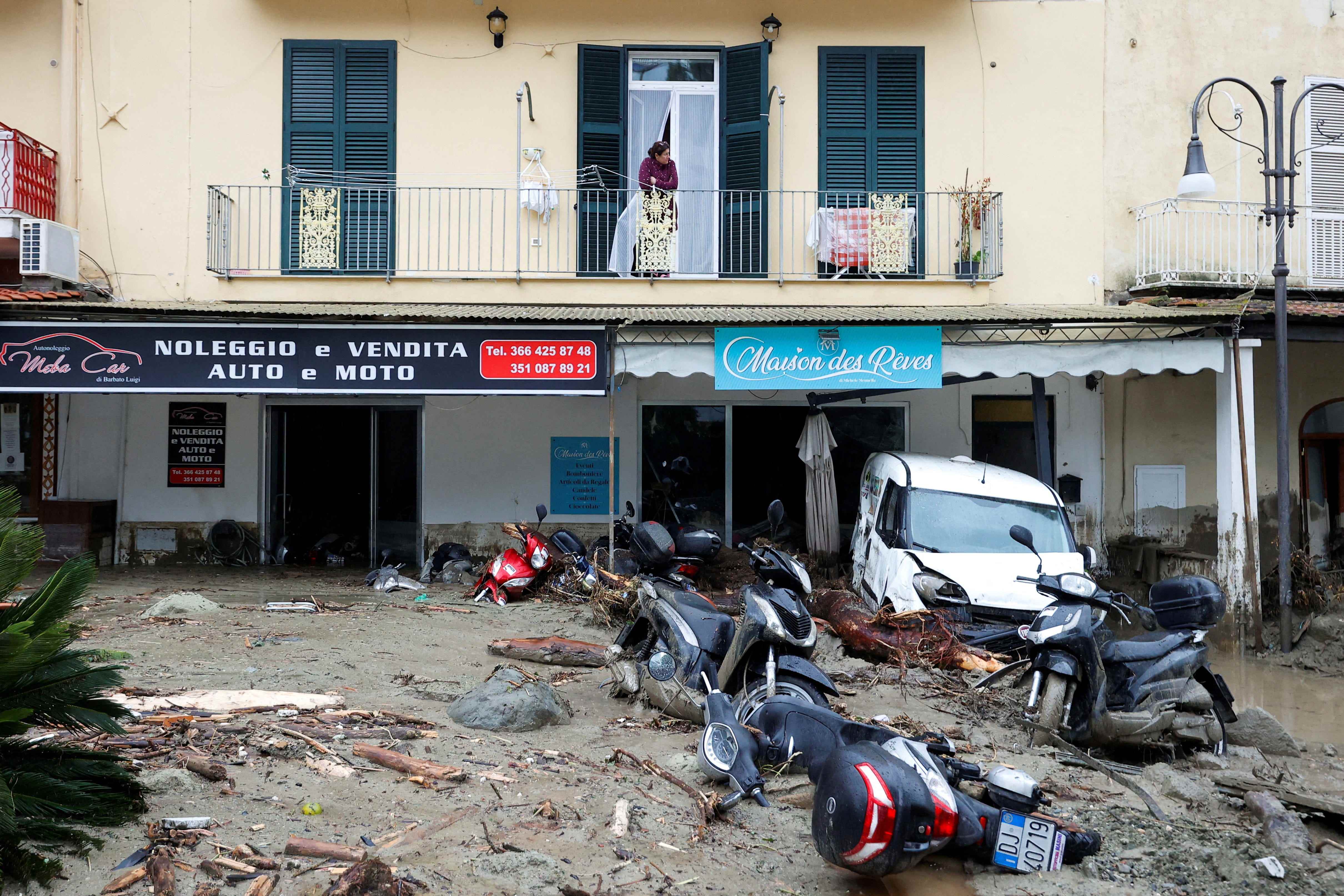 Eine Frau blickt von einem Balkon auf eine mit Trümmern und beschädigten Fahrzeugen bedeckte Straße nach einem Erdrutsch auf der italienischen Ferieninsel Ischia, Italien, 26. November 2022.