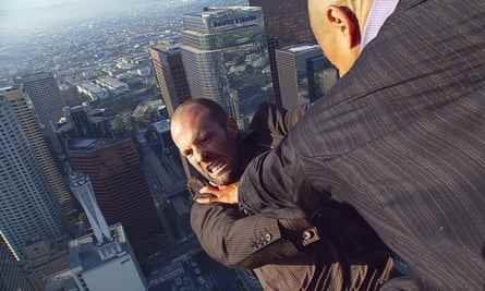 Ein Mann im Anzug, scheinbar ganz oben auf einem Gebäude, stößt Jason Statham an den Schultern