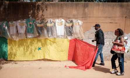 Ablaye Diaby hängt eine Flagge unter Dutzenden von Fußballtrikots an einer Wand gegenüber seinem kleinen Laden in Dakar auf.