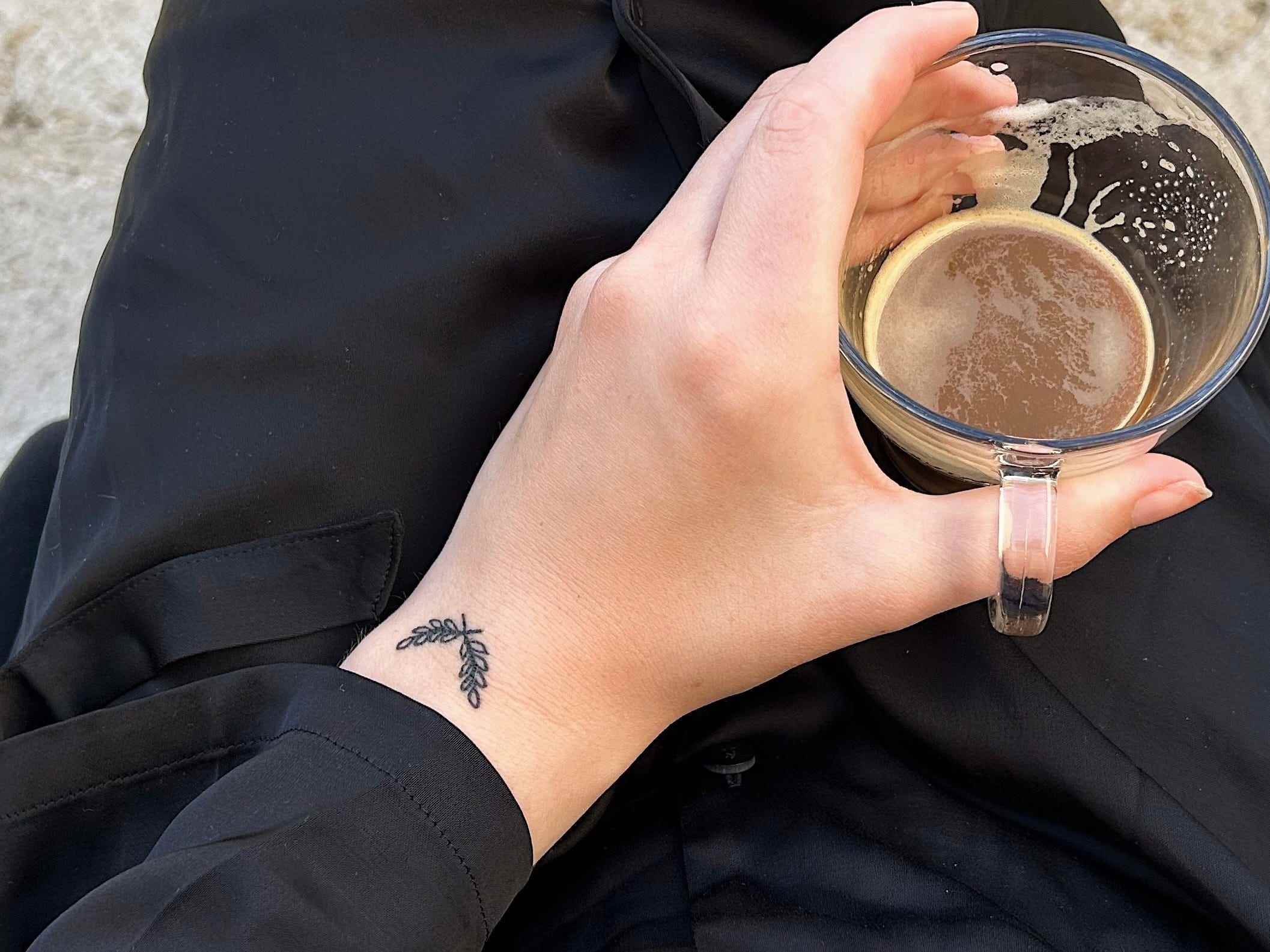 Der Autor hält eine Tasse Kaffee.  An ihrem Handgelenk ist ein Tattoo mit einem Olivenzweig zu sehen.