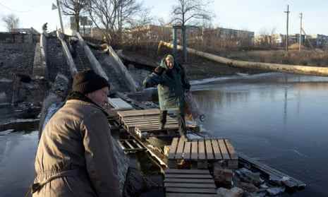 Eine ältere Frau mit einem Rollkoffer überquert am 4. Dezember den Fluss auf einer zerstörten Brücke in Bachmut, Gebiet Donezk.