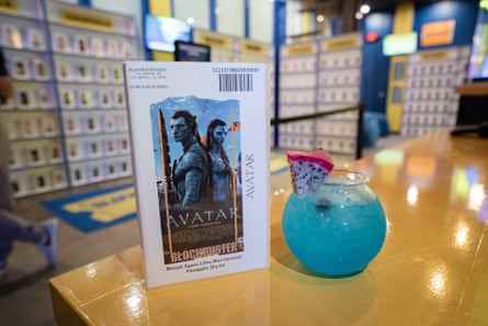 blaues Getränk in goldfischglasförmigem Glas neben Avatar-Videokoffer