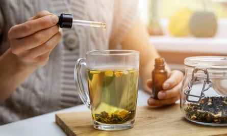 nahrungsergänzungsmittel und vitamine - frau, die tropfen cbd-öl in tasse tee mit pipette hinzufügt.