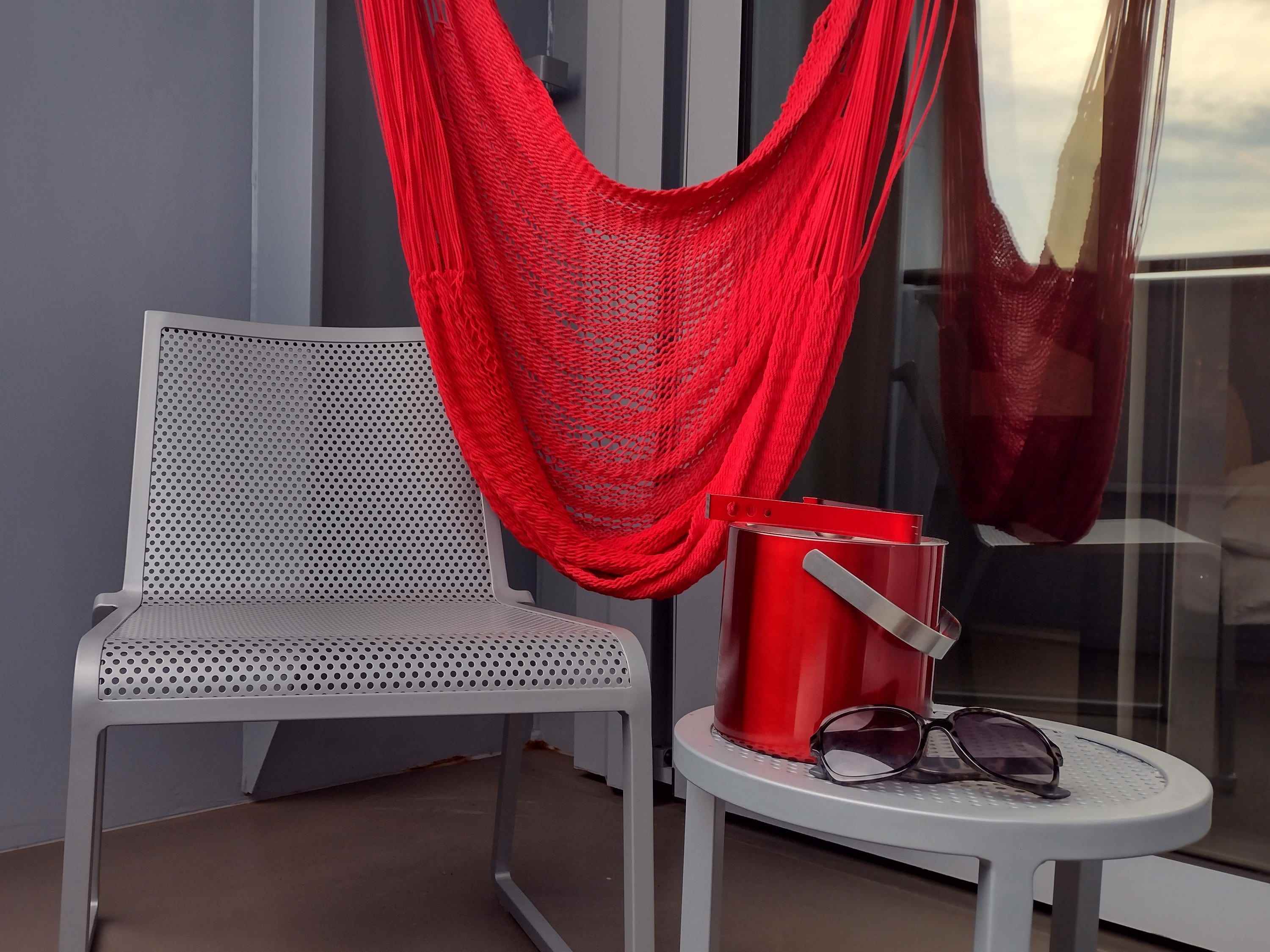 Ein Stuhl mit passendem Tisch und einem roten Eiskübel und einer drapierten hängenden roten Hängematte.