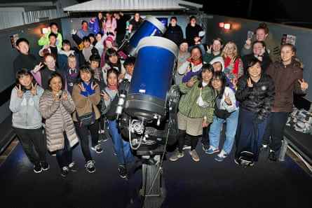 Eine Gruppe von Menschen steht nachts dicht gedrängt um ein großes Teleskop