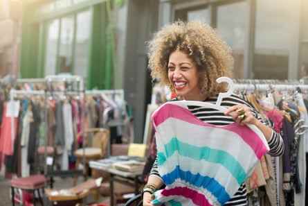 Eine Frau lacht, als sie ein Kleid auf einem Outdoor-Kleidermarkt hochhält.
