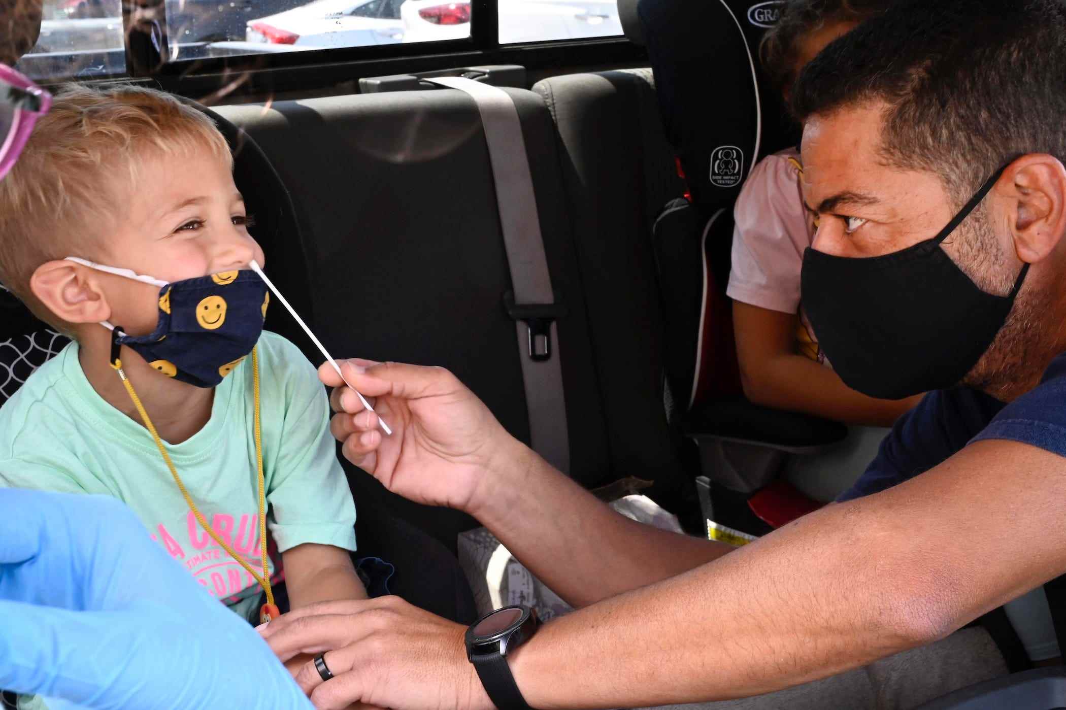 4-jähriger lächelt im autositz, während papa für einen schnelltest einen nasenabstrich an ihm durchführt