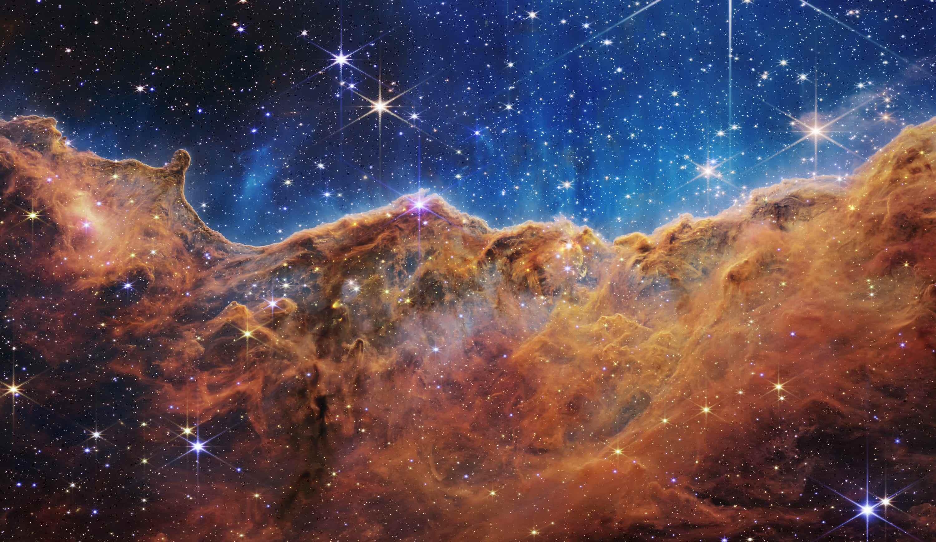 Carinanebel Sternentstehungsgebiet orangebraune Gas- und Staubwolken mit Sternen vor hellblauem Hintergrund