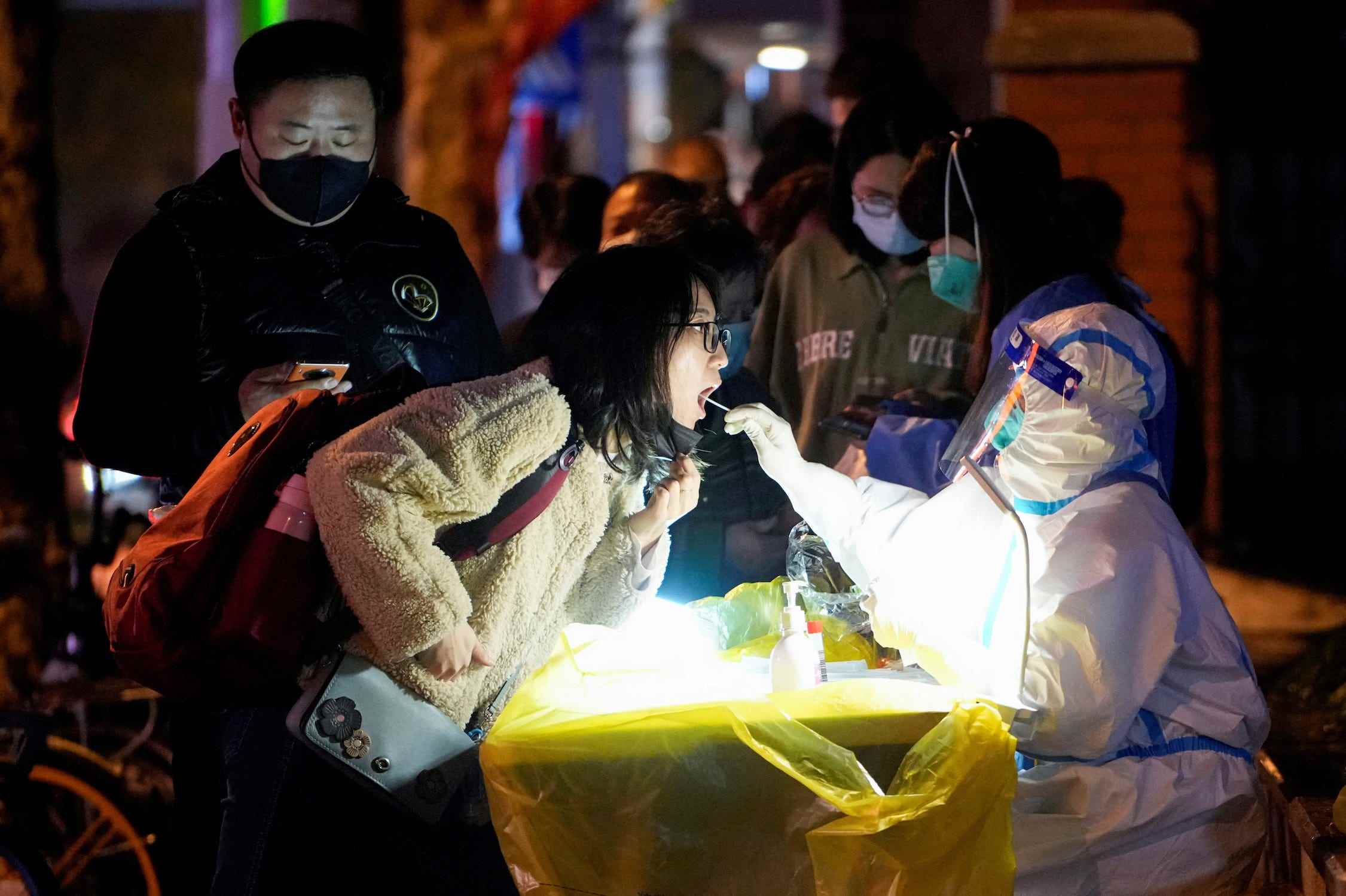 china covid arbeiter in biohazard anzug tupft frauen mund covid test mit schlange von wartenden leuten