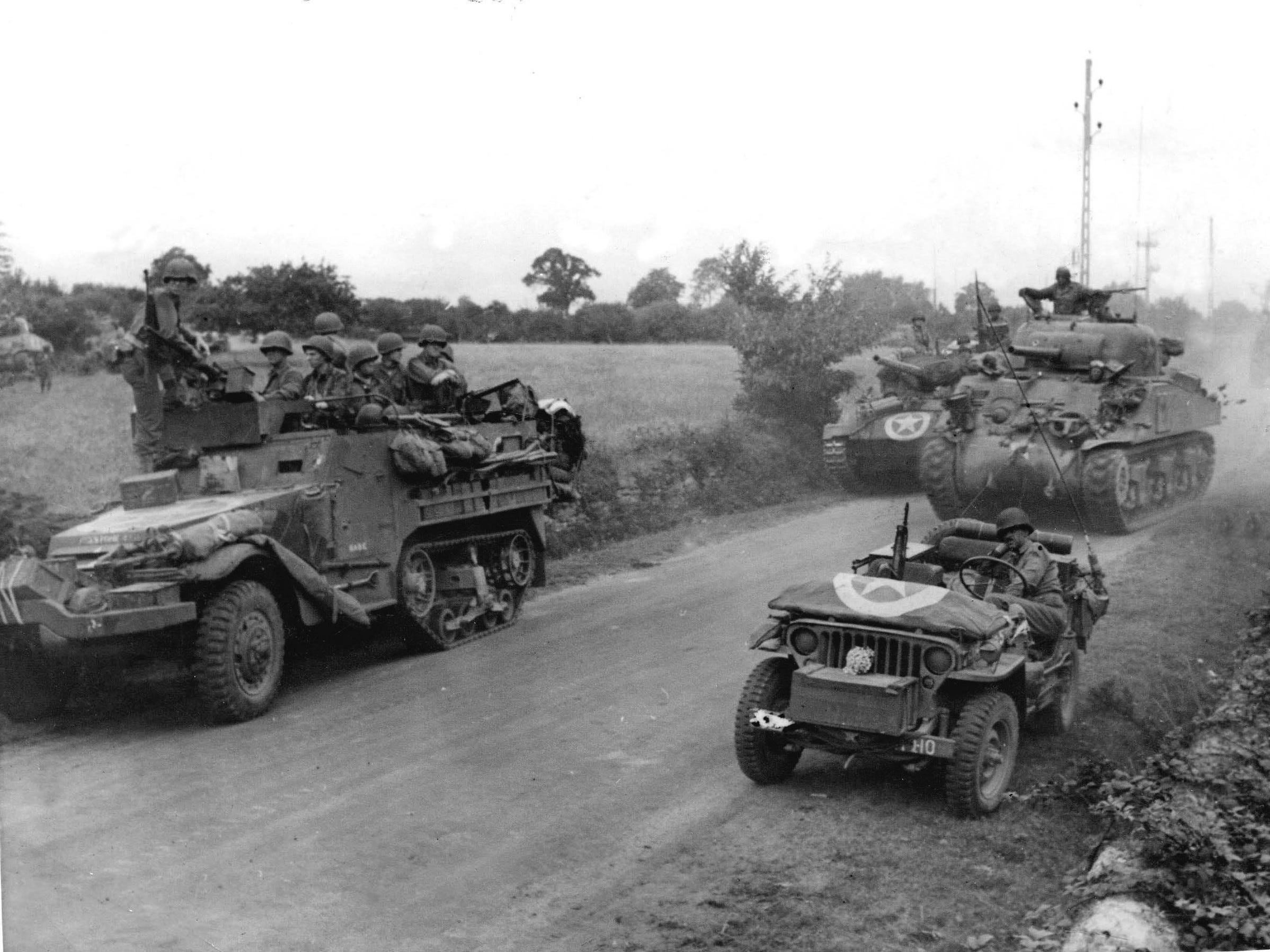 US-Soldaten in gepanzerten Fahrzeugen fahren während des Zweiten Weltkriegs auf einer Straße in der Bretagne, Frankreich