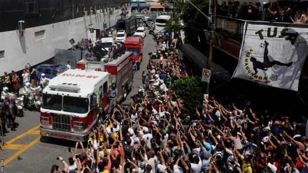 Peles Sarg wird auf einem Feuerwehrauto durch Santos eskortiert, wo Fans die Straßen säumen