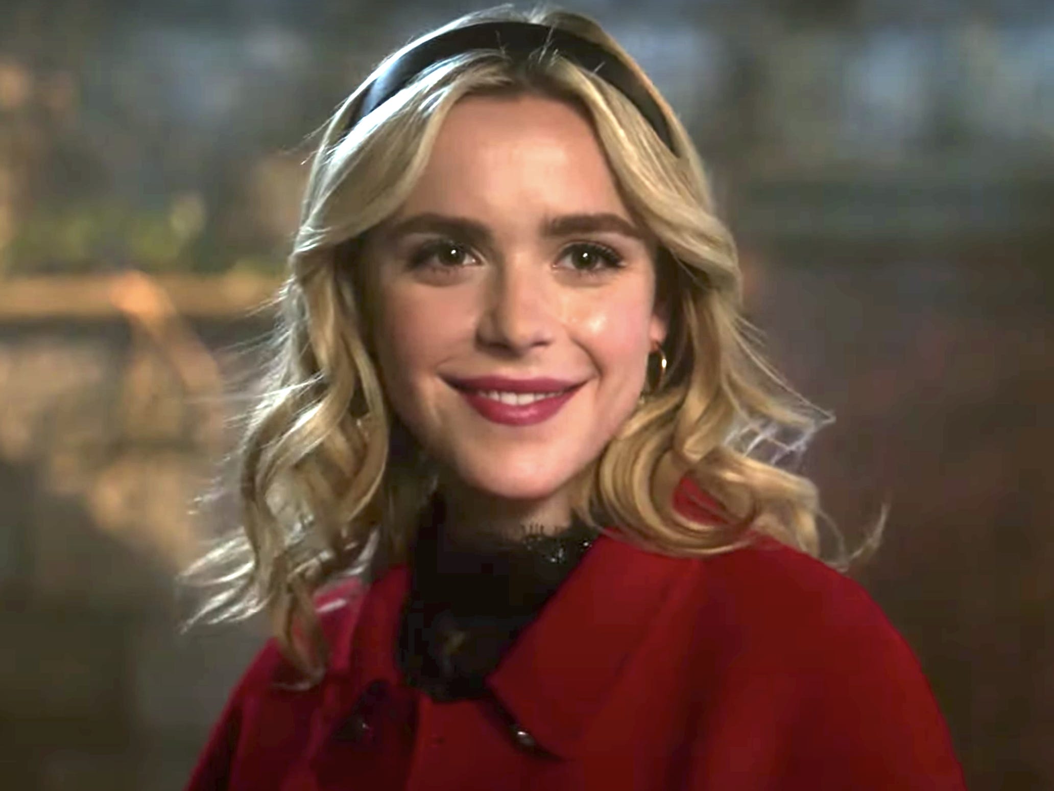 Kiernan Shipka trägt als Sabrina Spellman in „Riverdale“ ein schwarzes Stirnband und einen roten Mantel.