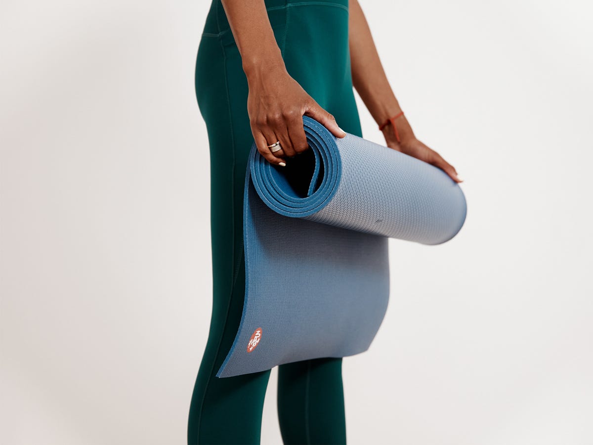 Eine Frau in grüner Hose, die eine zusammengerollte Maduka PRO 6 mm Yogamatte hält, die besten Yogamatten 2022