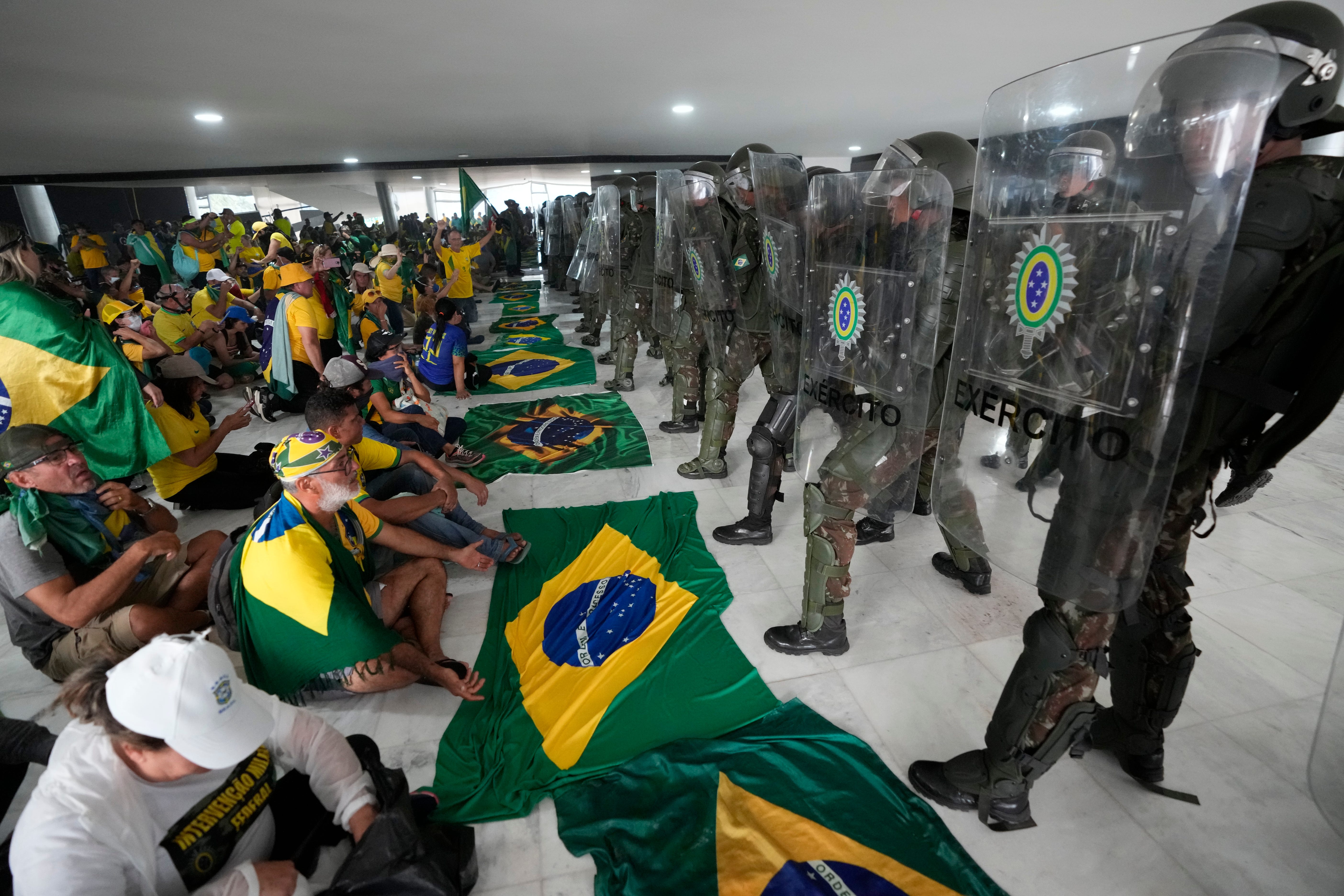Demonstranten, Unterstützer des ehemaligen brasilianischen Präsidenten Jair Bolsonaro, sitzen vor der Polizei, nachdem sie den Planalto-Palast gestürmt haben, in Brasilia, Brasilien, Sonntag, 8. Januar 2023.