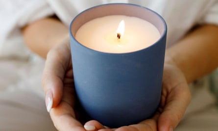 Eine brennende Kerze in einem blauen Keramikgefäß, das von zwei Händen gehalten wird.