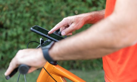Mann mit Handy an einem Mountainbike befestigt.  Außerdem trägt er eine Smartwatch.